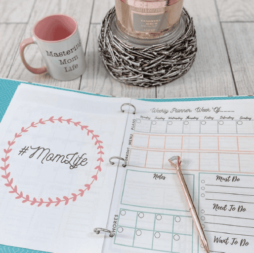 Mom planner printable in a binder, open to the weekly planner page next to a Mastering Mom Life mug